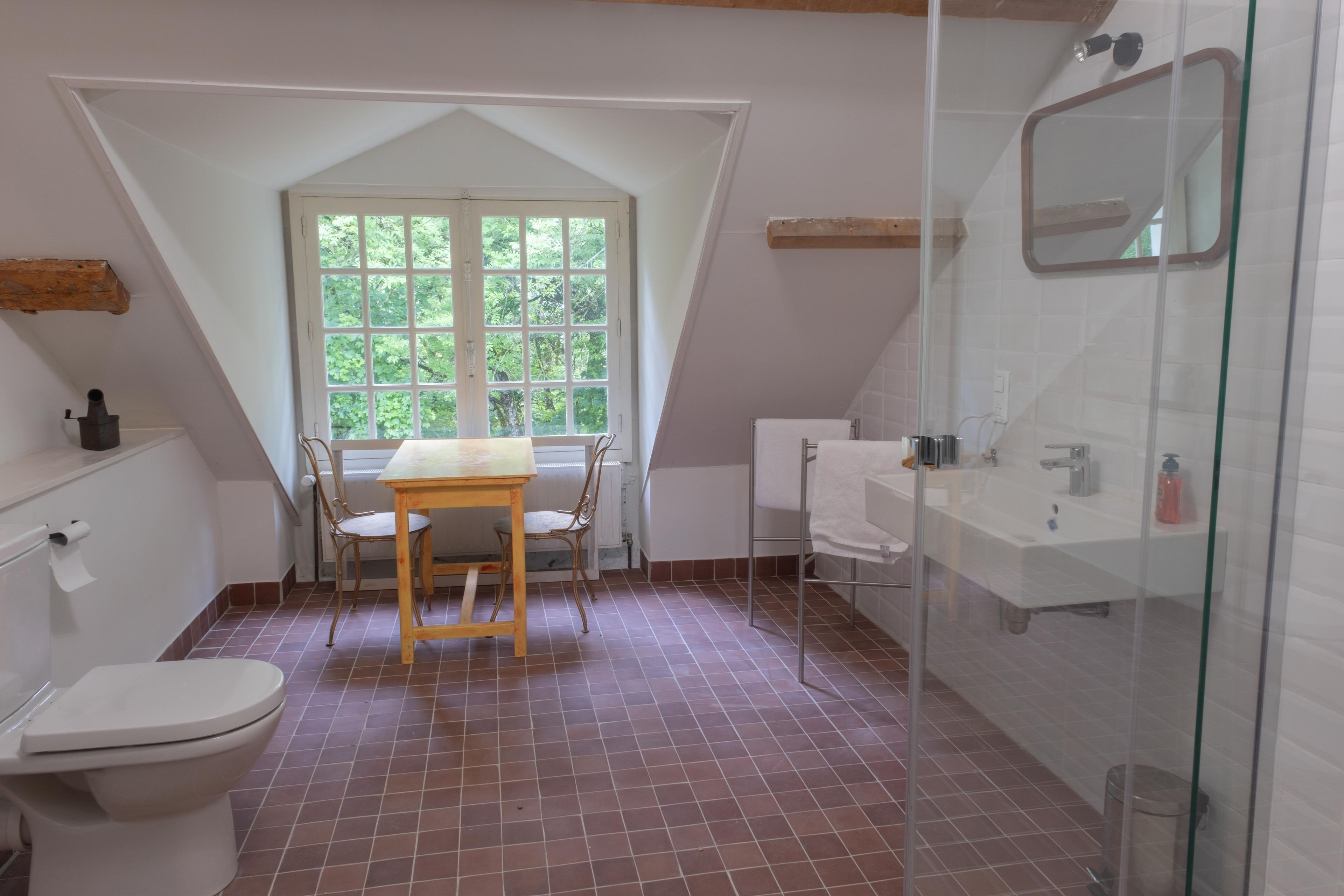 A bathroom with a shower, toilet, and a window with a view of greenery.