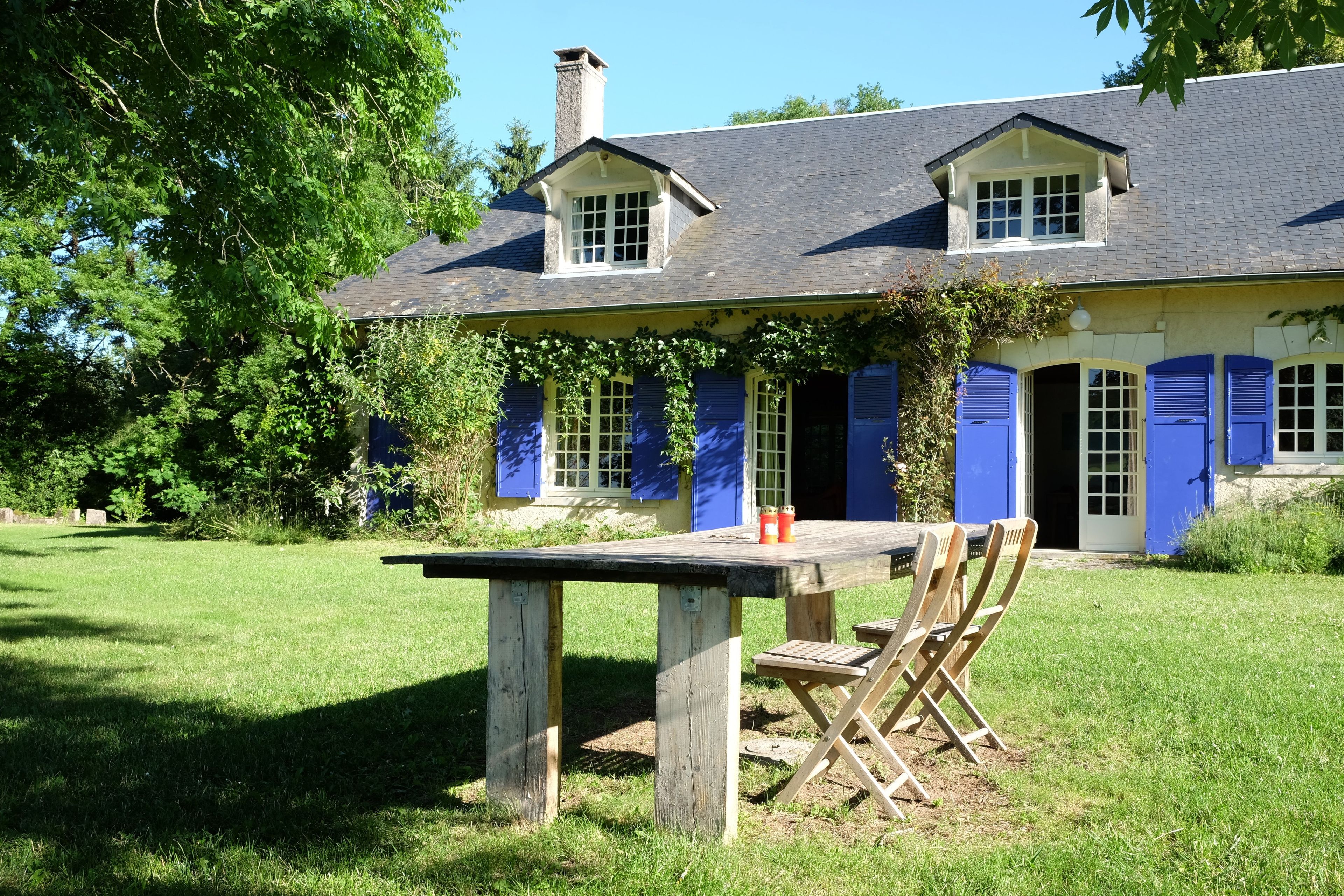 A house with a large front lawn, a dining table with chairs, and a chimney.