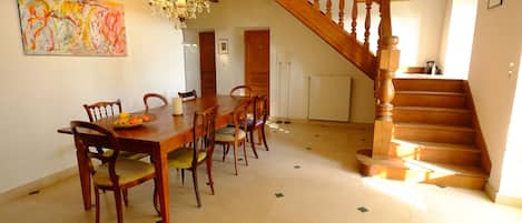 Un espace repas comprenant une table et des chaises en bois, un lustre et un escalier.
