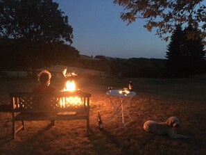 A bench with a fire, a table with a bottle and glass, and a dog lying nearby. - Spacious villa with private pool and panoramic views in the Morvan (Saint-Léger-de-Fougeret)