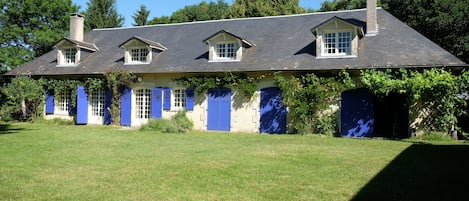 Ein zweigeschossiges Haus mit geneigtem Dach, mehreren Fenstern und blauen Fensterläden.
