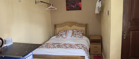 Une chambre à coucher comprenant un lit, une table de chevet, un porte-serviettes fixé au mur, un tableau et une petite armoire en bois.