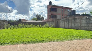 Un área pavimentada con un campo de césped, un muro de ladrillo y un edificio con un depósito de agua.