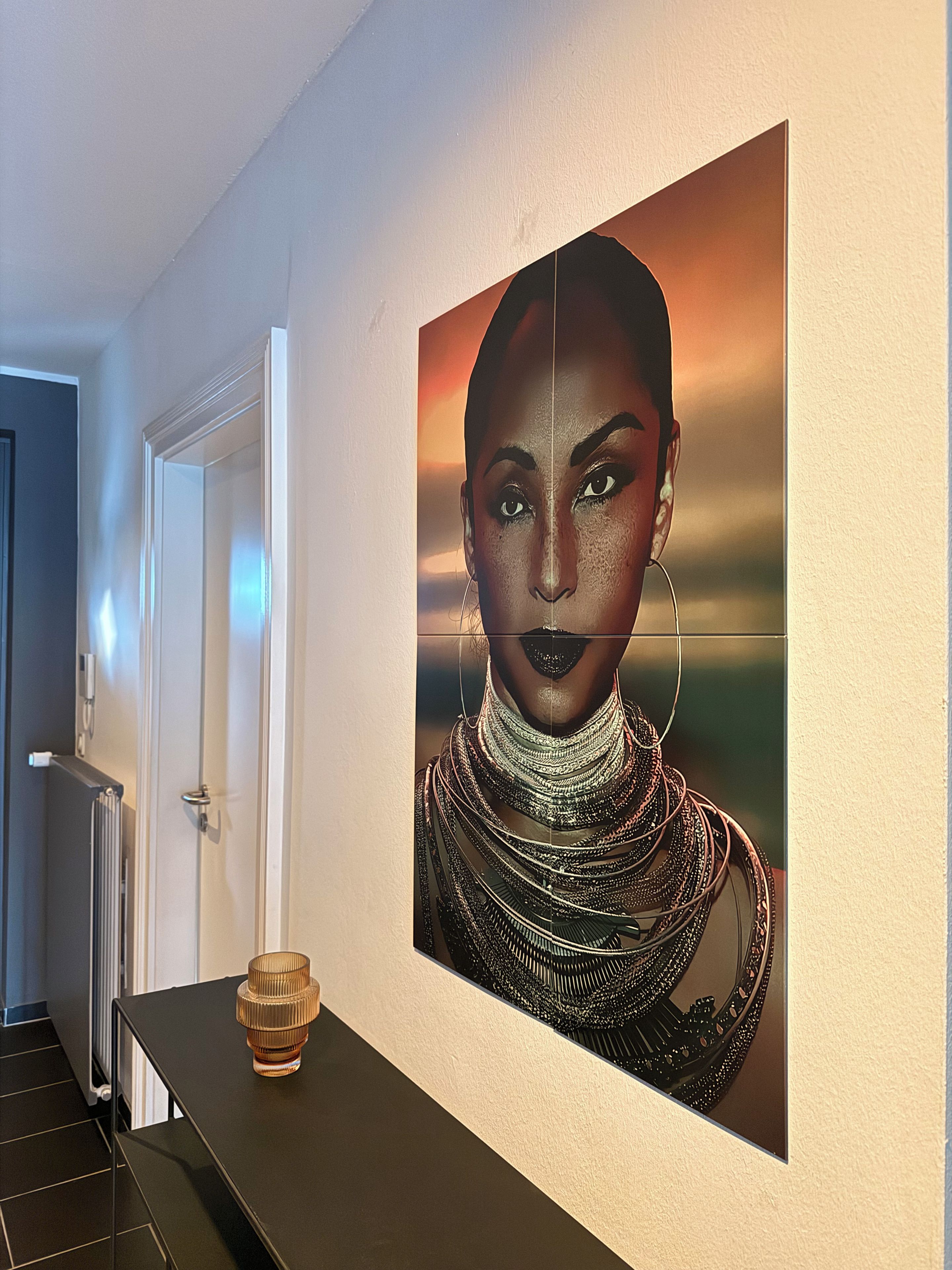 A hallway with a black table, a glass bottle, and a large framed artwork on the wall.