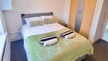 Een hotelkamer met een bed, nachtkastje, lamp, kast en een radiator.