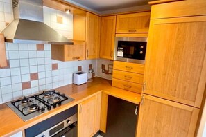 A compact kitchen with wooden cabinets, a gas stove, a built-in oven, and a microwave.