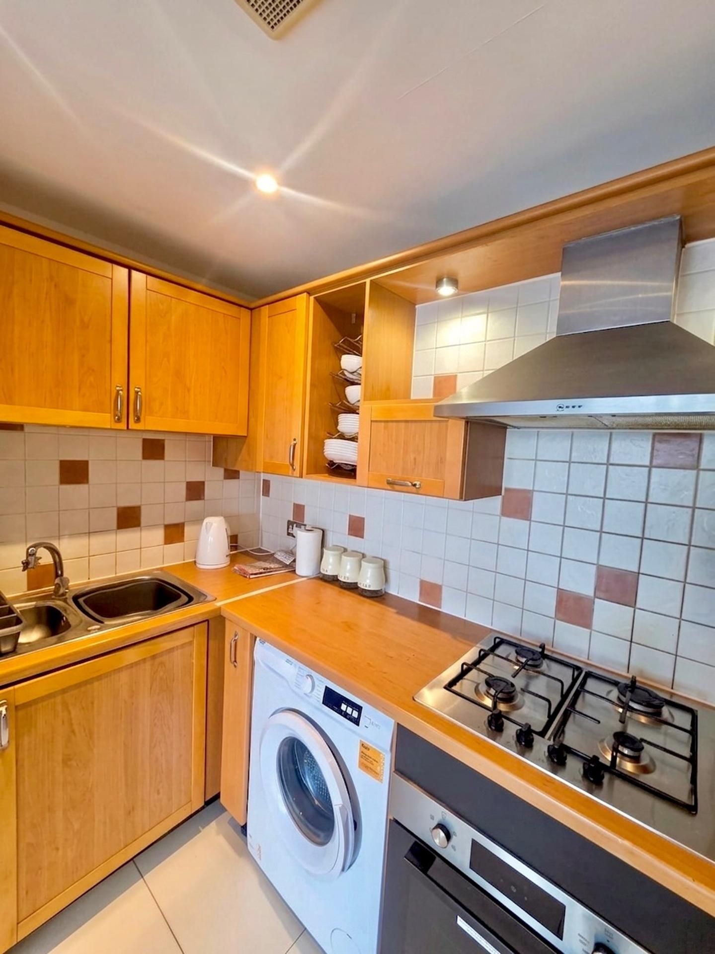 Una cocina compacta con armarios de madera, lavadora integrada, estufa a gas y salpicadero de azulejos.