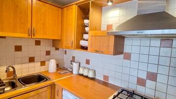 Una cocina compacta con armarios de madera, lavadora integrada, estufa a gas y salpicadero de azulejos.