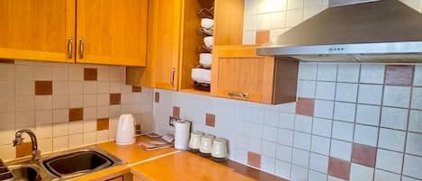 A compact kitchen with wooden cabinets, a built-in washing machine, a gas stove, and a tiled backsplash.