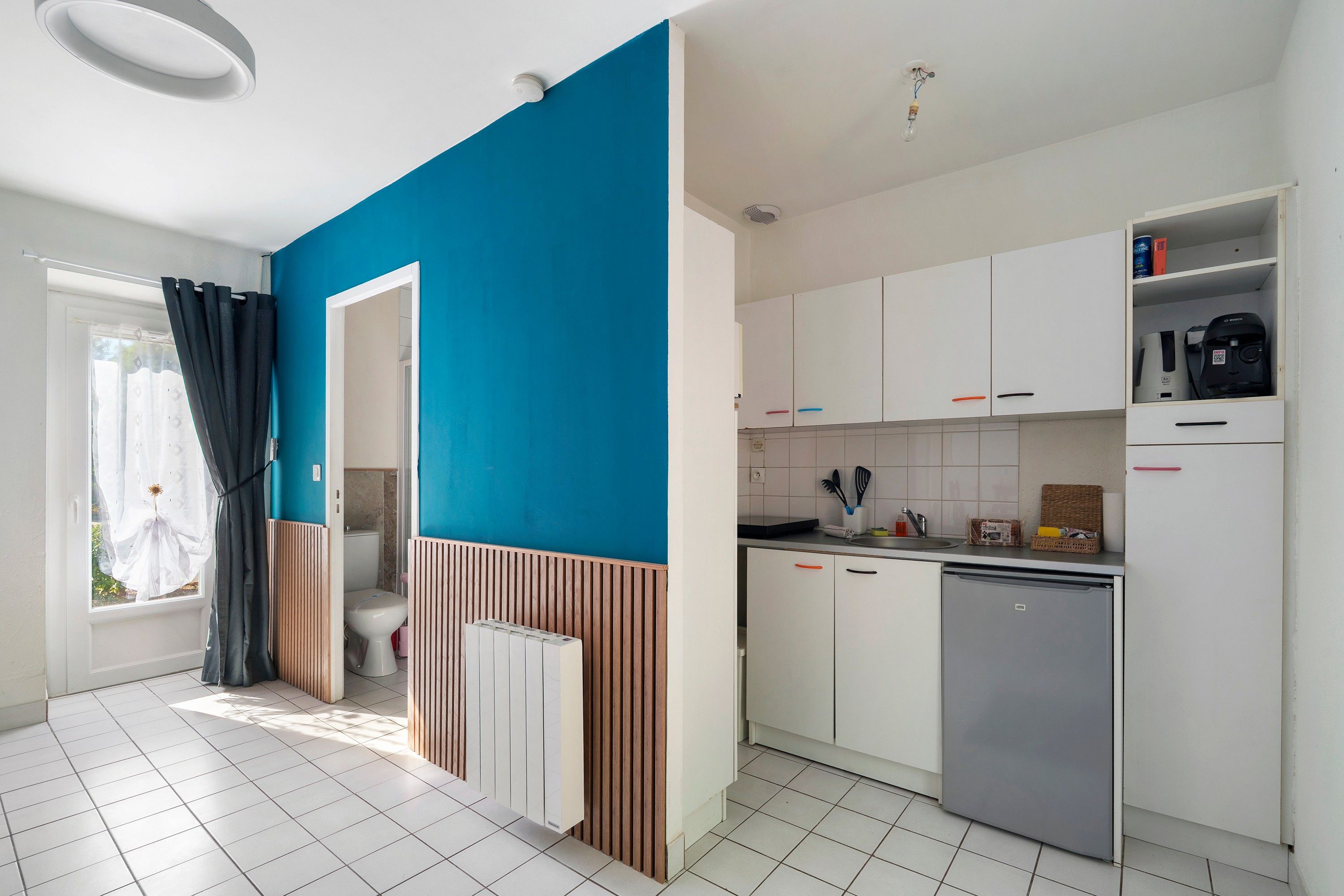 A modern kitchen with white cabinets, a dishwasher, and a blue accent wall.