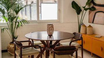Un coin repas comprenant une table ronde, quatre chaises, un centre de table en fibres tressées et un buffet jaune agrémenté d’objets décoratifs.
