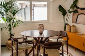 Zona pranzo con tavolo rotondo, quattro sedie, centrotavola intrecciato e un armadietto giallo con oggetti decorativi.