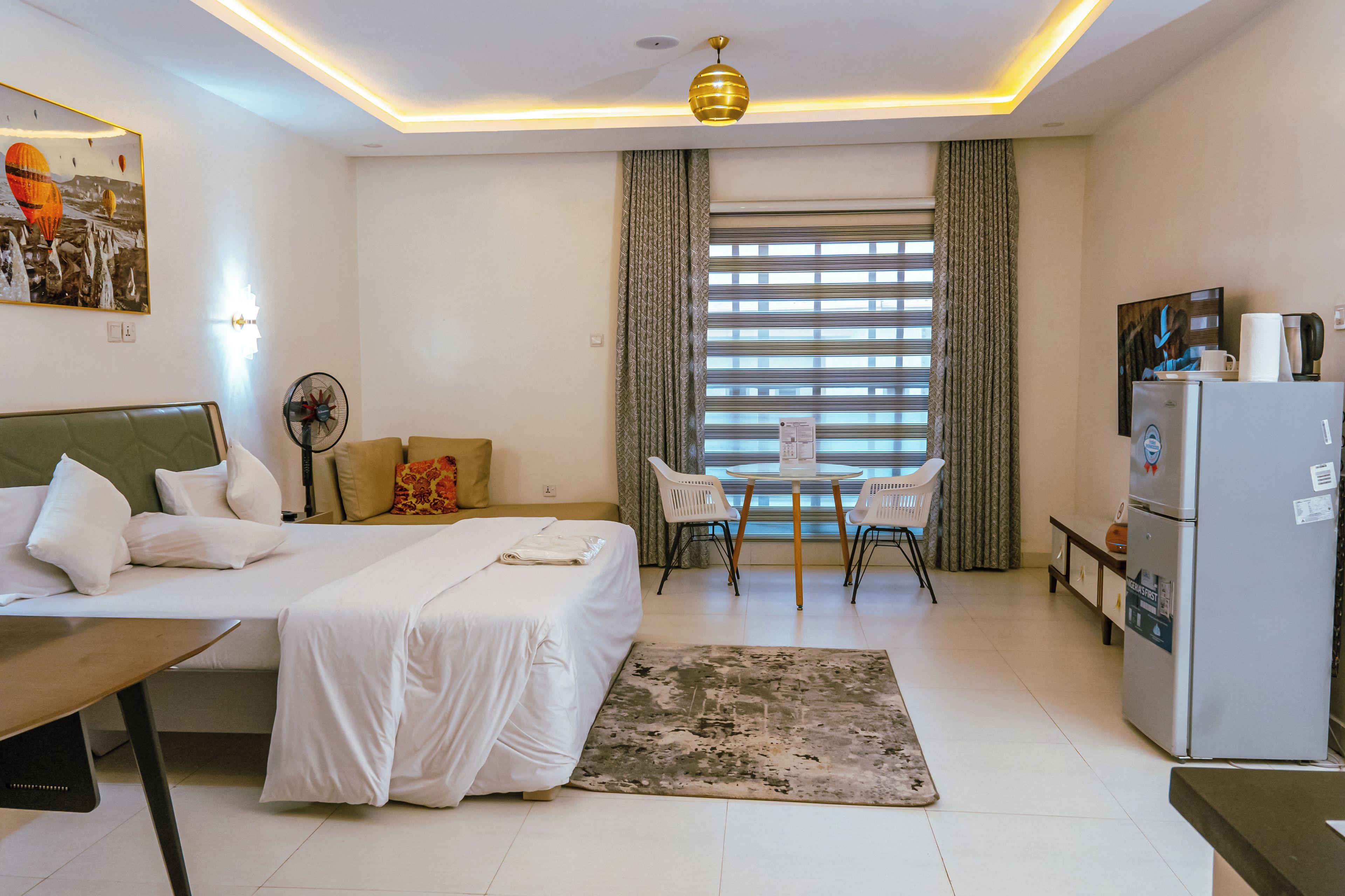 A hotel room with a bed, a desk, a chair, a refrigerator, and a window with curtains.