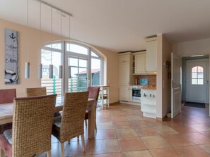 A spacious kitchen with white cabinets, a dining area with wicker chairs, and a large window providing natural light. - Holiday Home With 1 Bedroom (St. Peter-Ording)