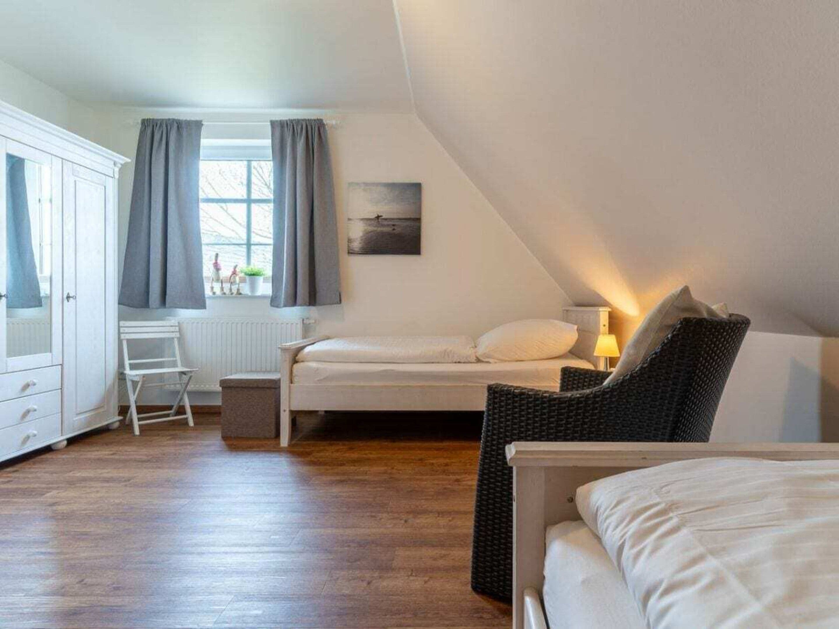 A bedroom with a bed, a chair, a desk, and a window with curtains.