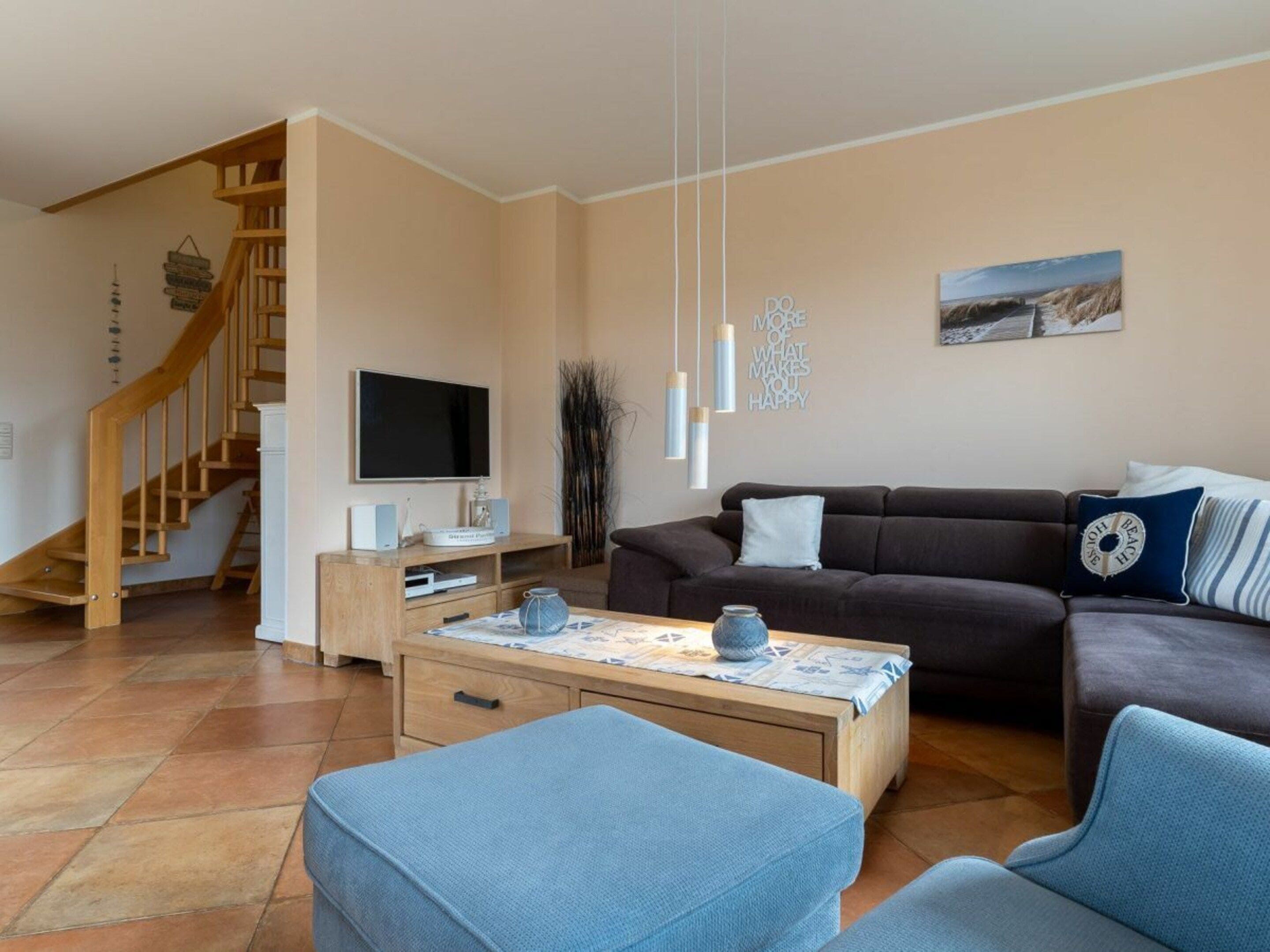 A living room with a sofa, coffee table, and chairs, a TV, and a staircase.
