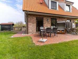 A brick house with a tiled roof, a patio with a table and chairs, and a stone wall. - Holiday Home With 1 Bedroom (St. Peter-Ording)