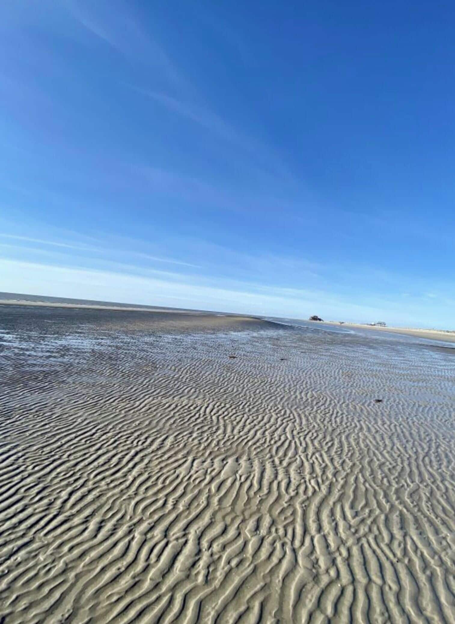 A beach with rippled sand patterns under a clear blue sky.