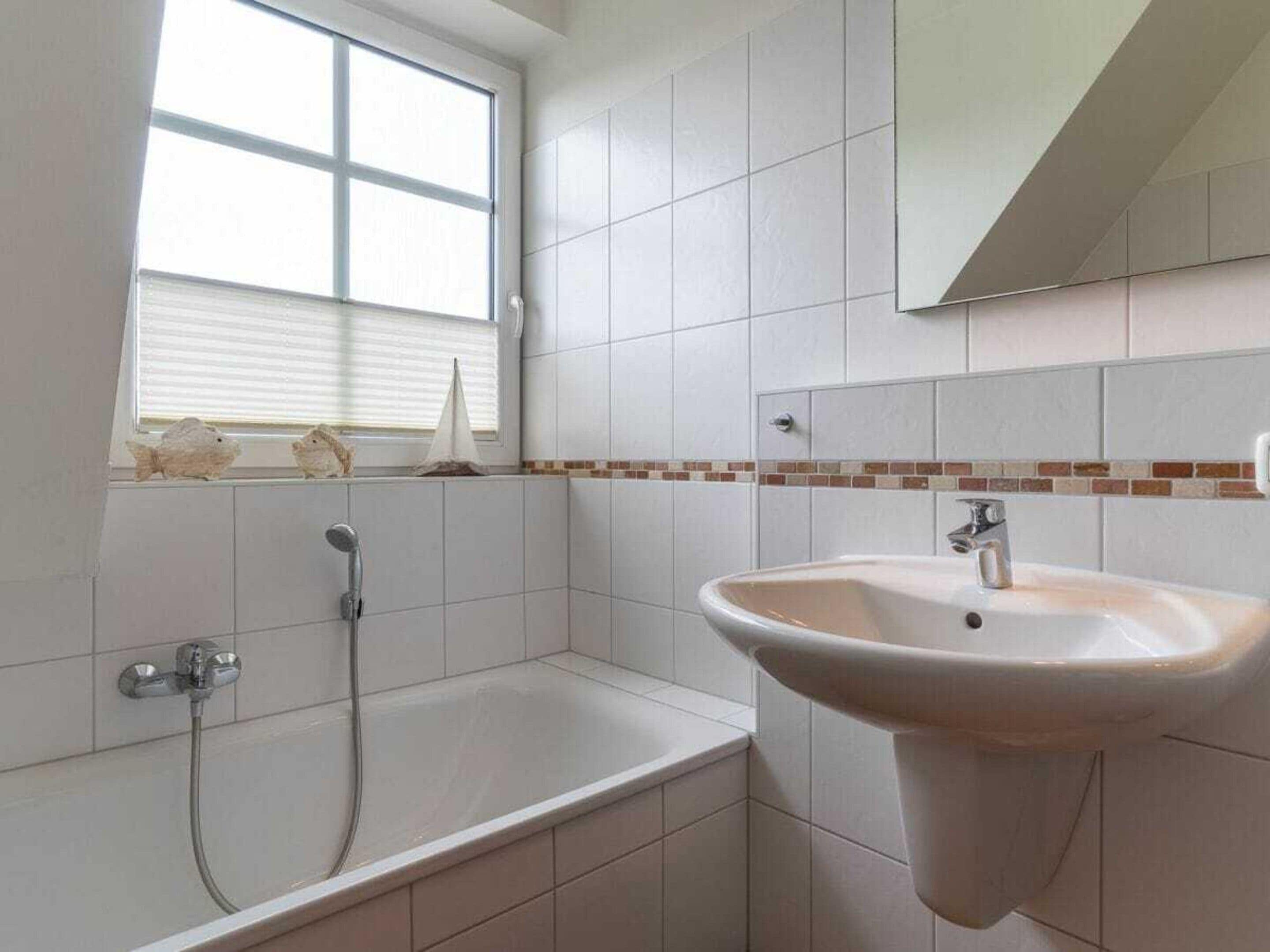 A bathroom with a bathtub, a sink, and a window with blinds.