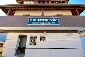A building with a sign for 'Werneck Residence Suites' and contact numbers.
