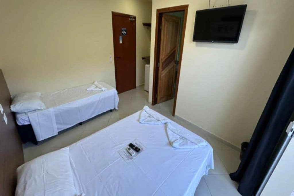 Een hotelkamer met twee eenpersoonsbedden, een televisie aan de muur en een deur naar een andere kamer.