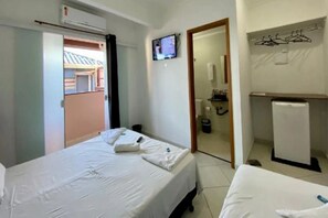 Une chambre d’hôtel avec deux lits, une télévision, un petit réfrigérateur et une porte donnant sur un balcon.