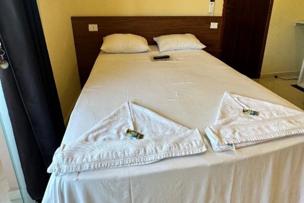 A neatly made bed with pillows and a remote control on it.