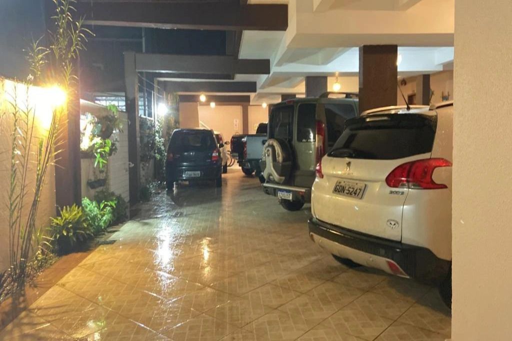 Un garaje de estacionamiento con varios coches aparcados, suelo mojado y una planta a la izquierda.