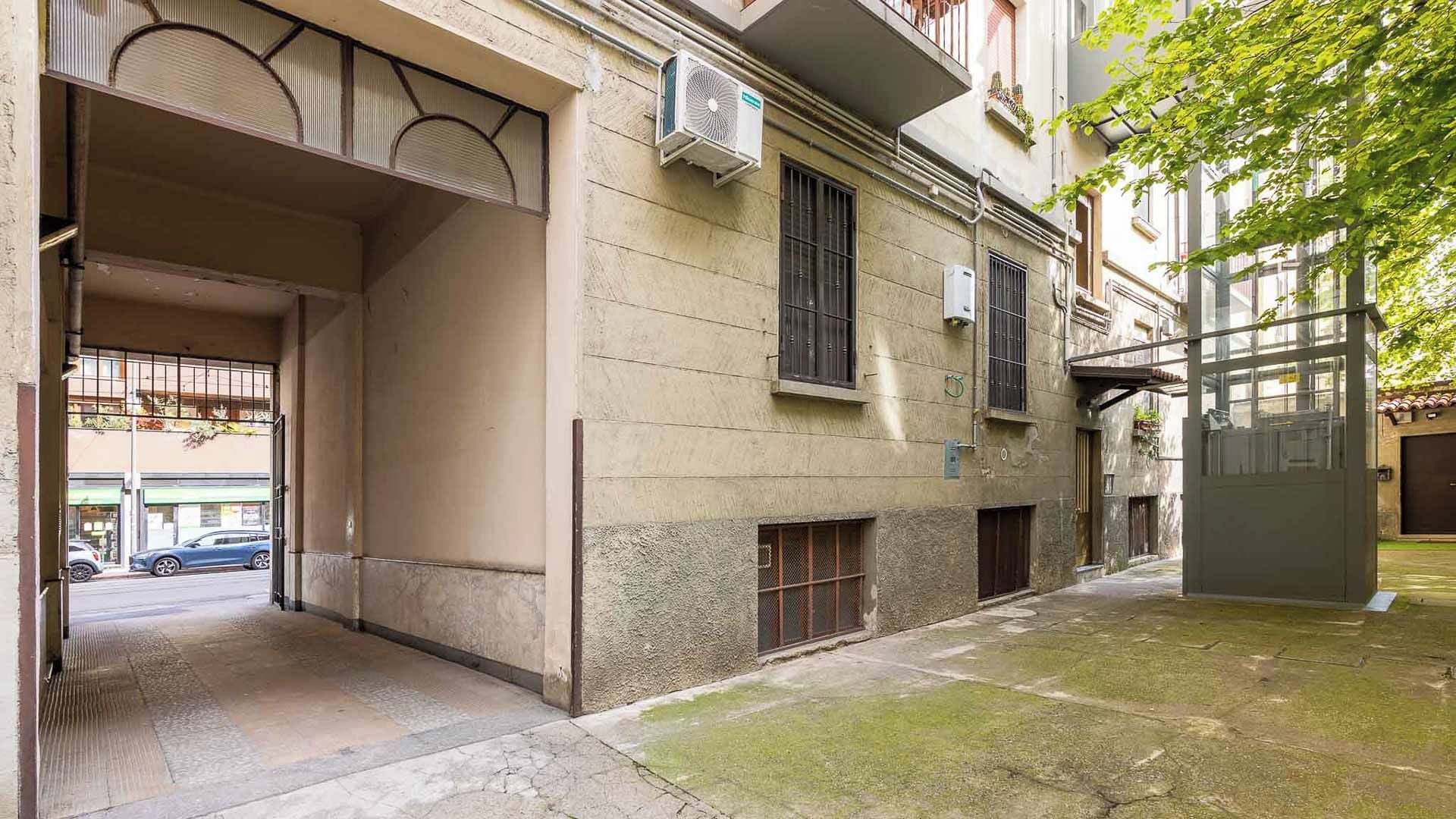 A building with a covered entrance, air conditioning units, and a small garden area.