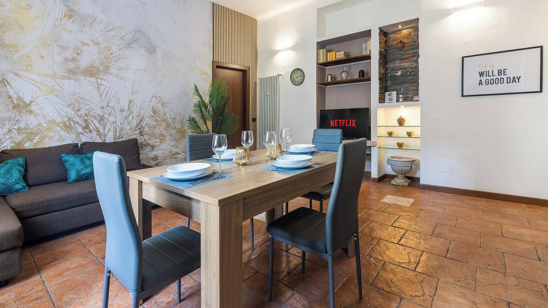Zona pranzo con tavolo in legno apparecchiato per quattro persone, una poltrona e un cartello Netflix a parete.