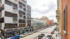 Un edificio de varios pisos con balcones, una calle con coches aparcados y un cielo despejado.