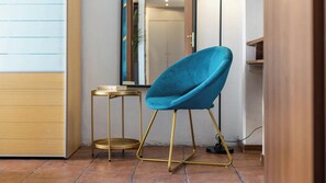 Una habitación con una silla azul, una mesita redonda y un espejo en la pared.
