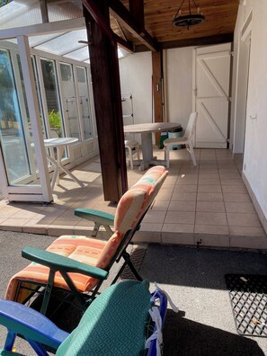 A covered outdoor seating area with chairs and a table, a glass door entrance, and a white door in the background. - A 5-minute drive from the beach at Lac d'Hossegor Park, the golf course, and downtown (Soorts-Hossegor)