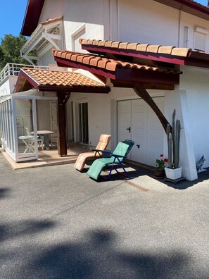 A covered outdoor seating area with two lounge chairs and a table, a white building with a red-tiled roof, and a cactus plant. - A 5-minute drive from the beach at Lac d'Hossegor Park, the golf course, and downtown (Soorts-Hossegor)
