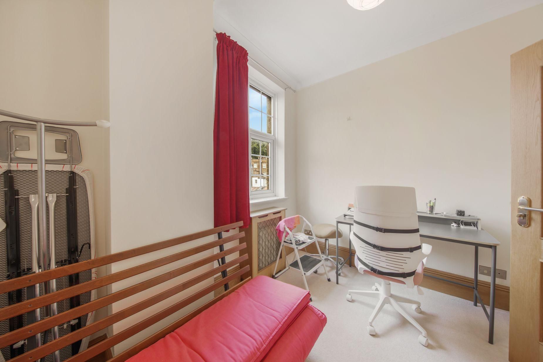A bedroom with a bed, a desk, a chair, and a window with curtains.