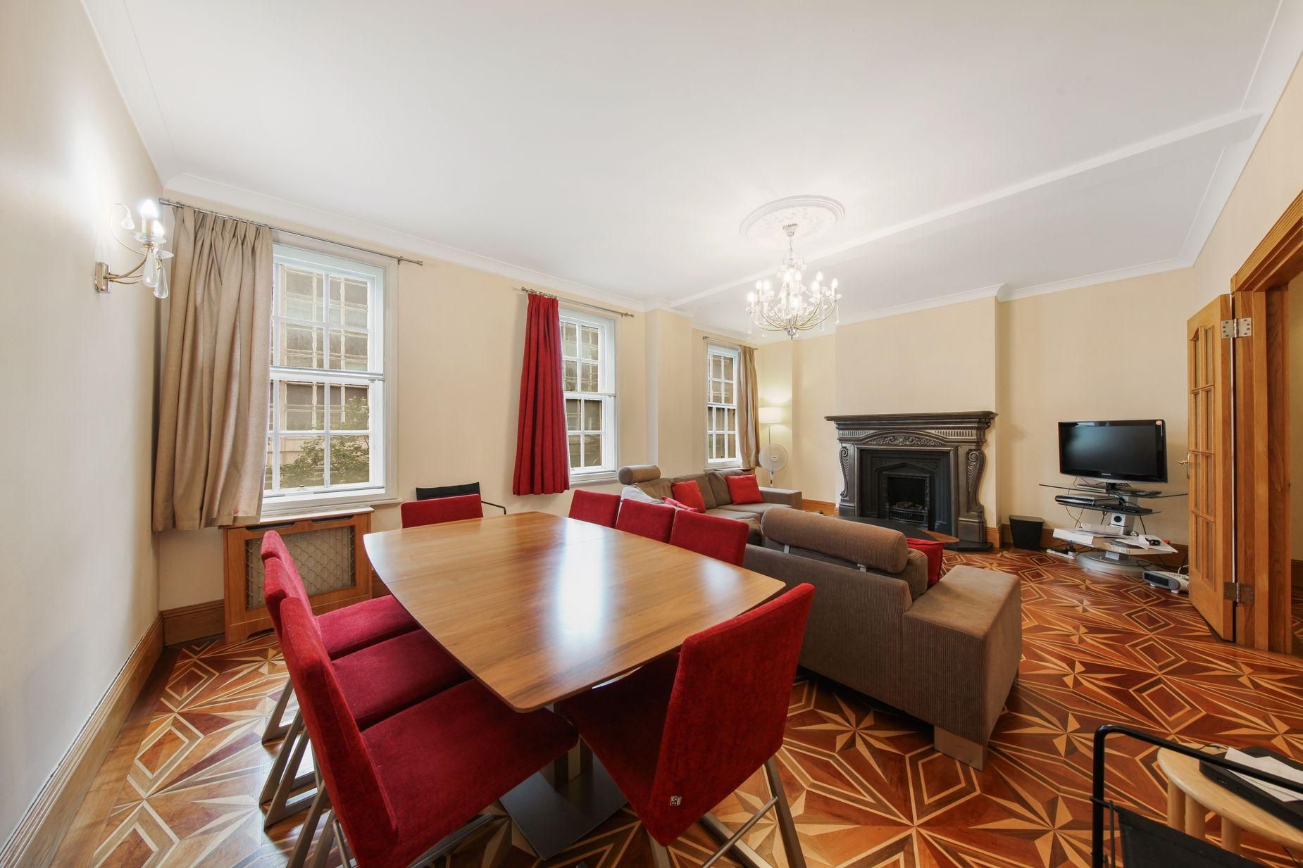 A room with a dining table, red chairs, a sofa, a television, and a fireplace.