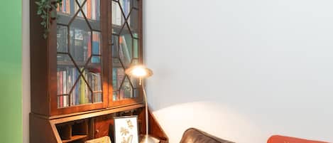 Une bibliothèque en bois avec des portes en verre, une lampe de bureau, un tableau encadré et un canapé en cuir.
