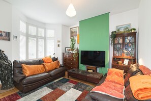 A living room with a leather sofa, a television, a green accent wall, and a bookshelf. - Stylish & Artistic 3-Bedroom, garden, London Home - Pass the Keys (London)