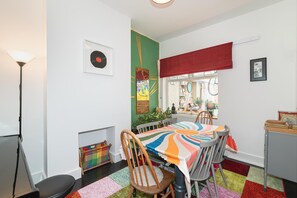 A dining area with a colorful tablecloth, chairs, a floor lamp, a framed record, and a green wall with a poster. - Stylish & Artistic 3-Bedroom, garden, London Home - Pass the Keys (London)