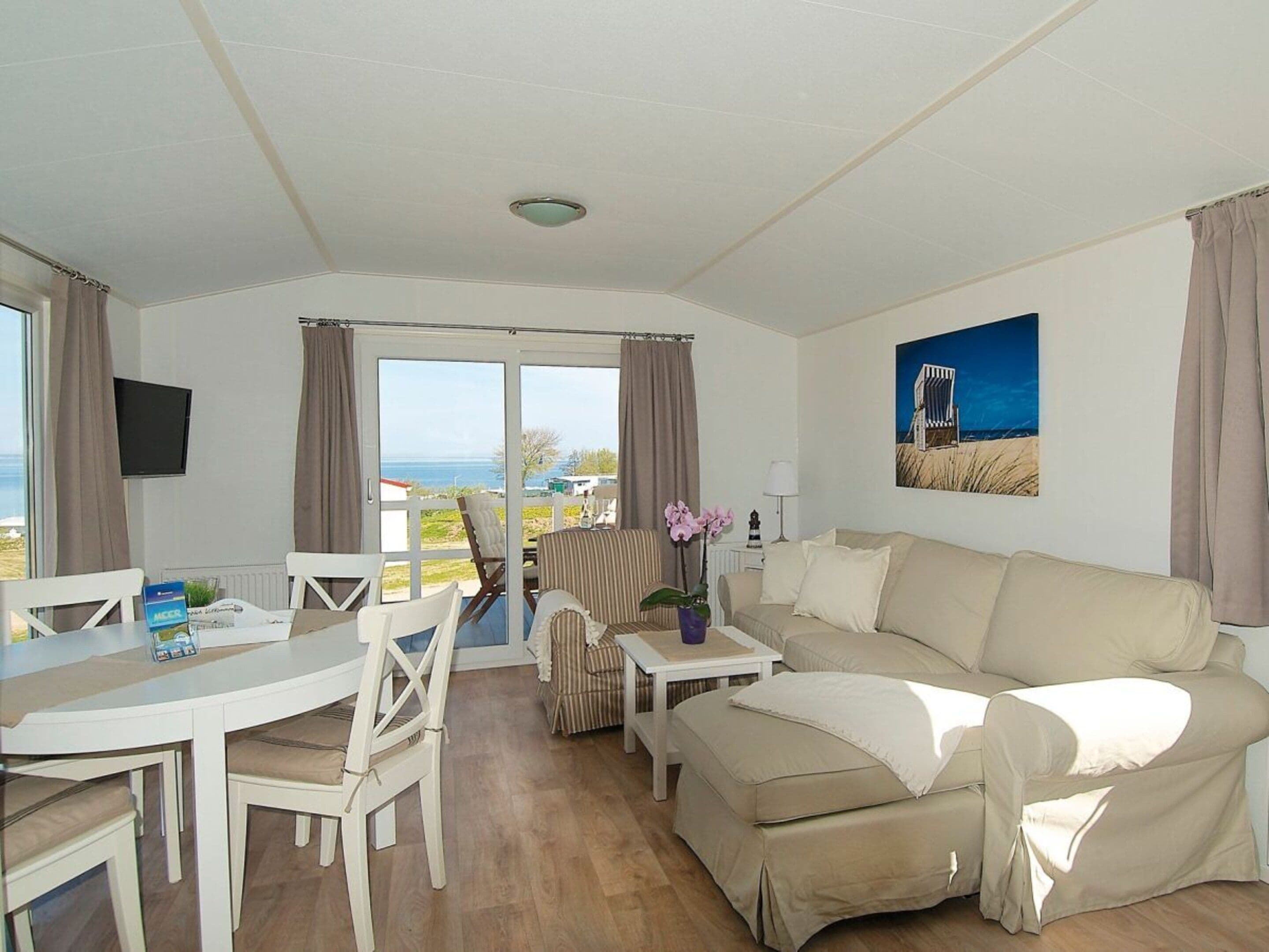 A room with a sofa, a dining table, chairs, a TV, and a view of the sea.