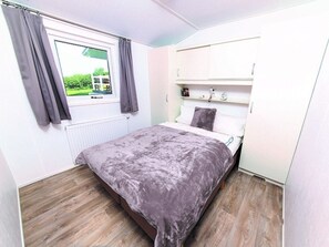 Ein Schlafzimmer mit Bett, einem Fenster mit Vorhängen, einem Heizkörper und einem weißen Kleiderschrank.