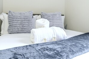 A neatly made bed with a grey textured blanket, two grey pillows, and a white towel rolled up. - Roundhay Retreat – Family-Friendly Home + Parking - Pass the Keys (Leeds)