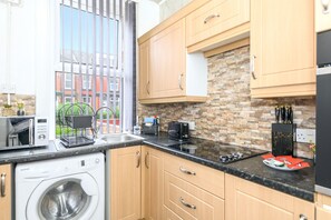 A modern kitchen with wooden cabinets, a built-in washing machine, a toaster, and a stone backsplash. - Roundhay Retreat – Family-Friendly Home + Parking - Pass the Keys (Leeds)