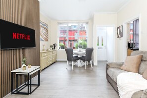 A modern living room with a flat-screen TV, a dining area with a table and chairs, and a sofa. - Roundhay Retreat – Family-Friendly Home + Parking - Pass the Keys (Leeds)