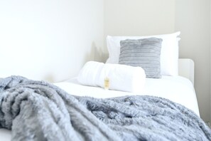 Una cama con ropa de cama blanca, un edredón gris y una almohada con una etiqueta.