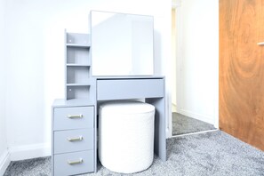 Een grijze wastafel met spiegel, twee lades en een rond krukje.
