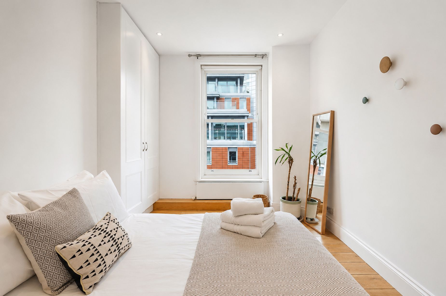 A bedroom with a bed, pillows, a window, a mirror, and a view of a building.
