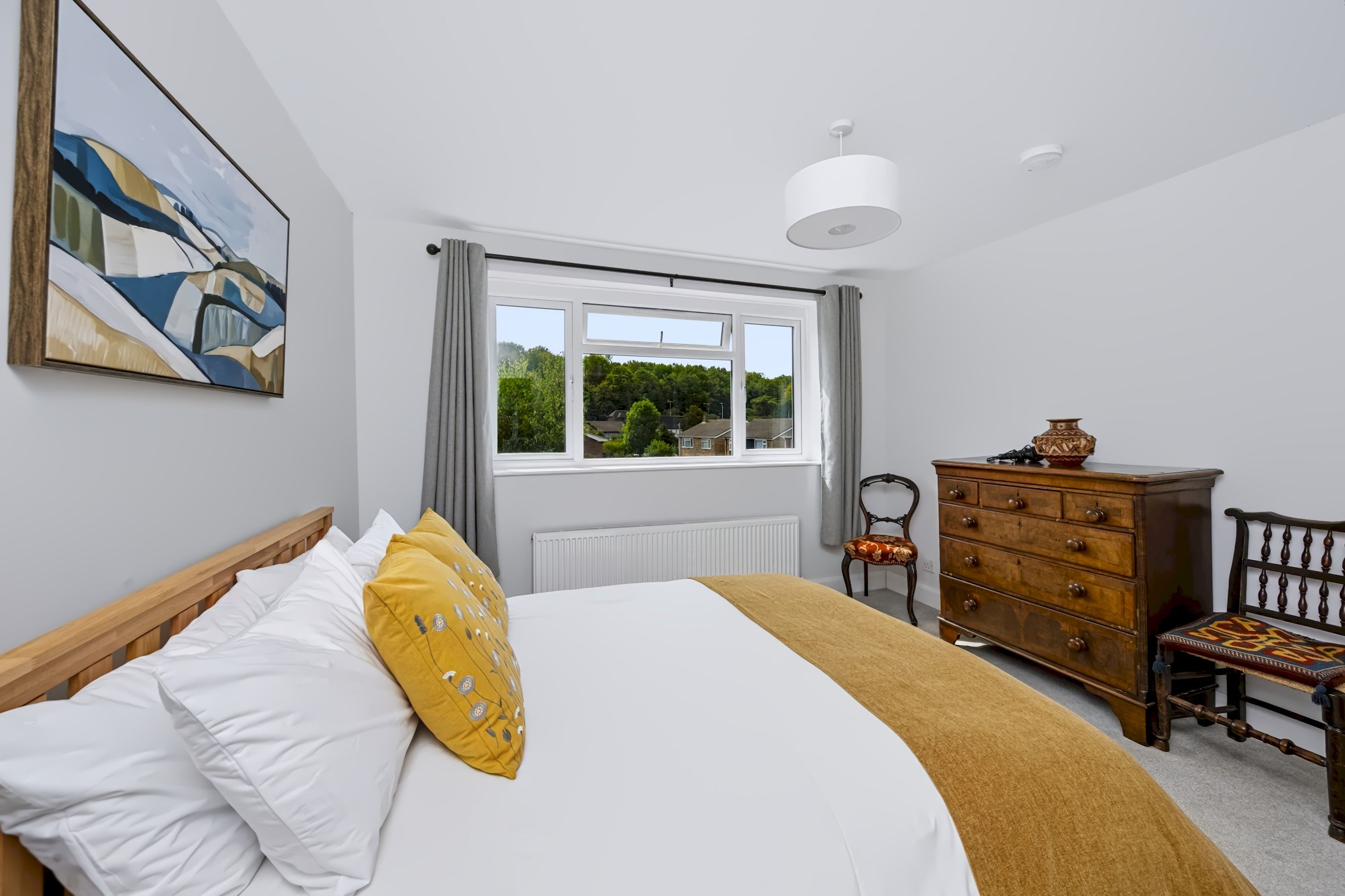 A bedroom with a bed, a dresser, a chair, and a window with a view of greenery.