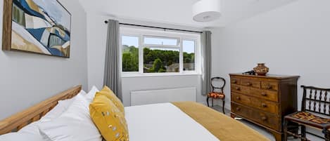 A bedroom with a bed, a dresser, a chair, and a window with a view of greenery.