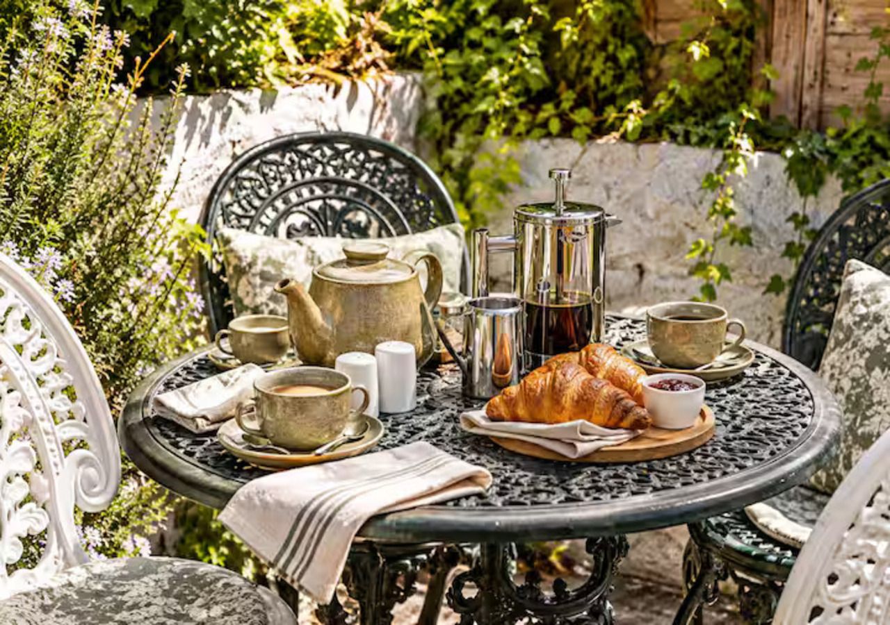 A round metal table with a croissant, coffee cups, and a teapot.